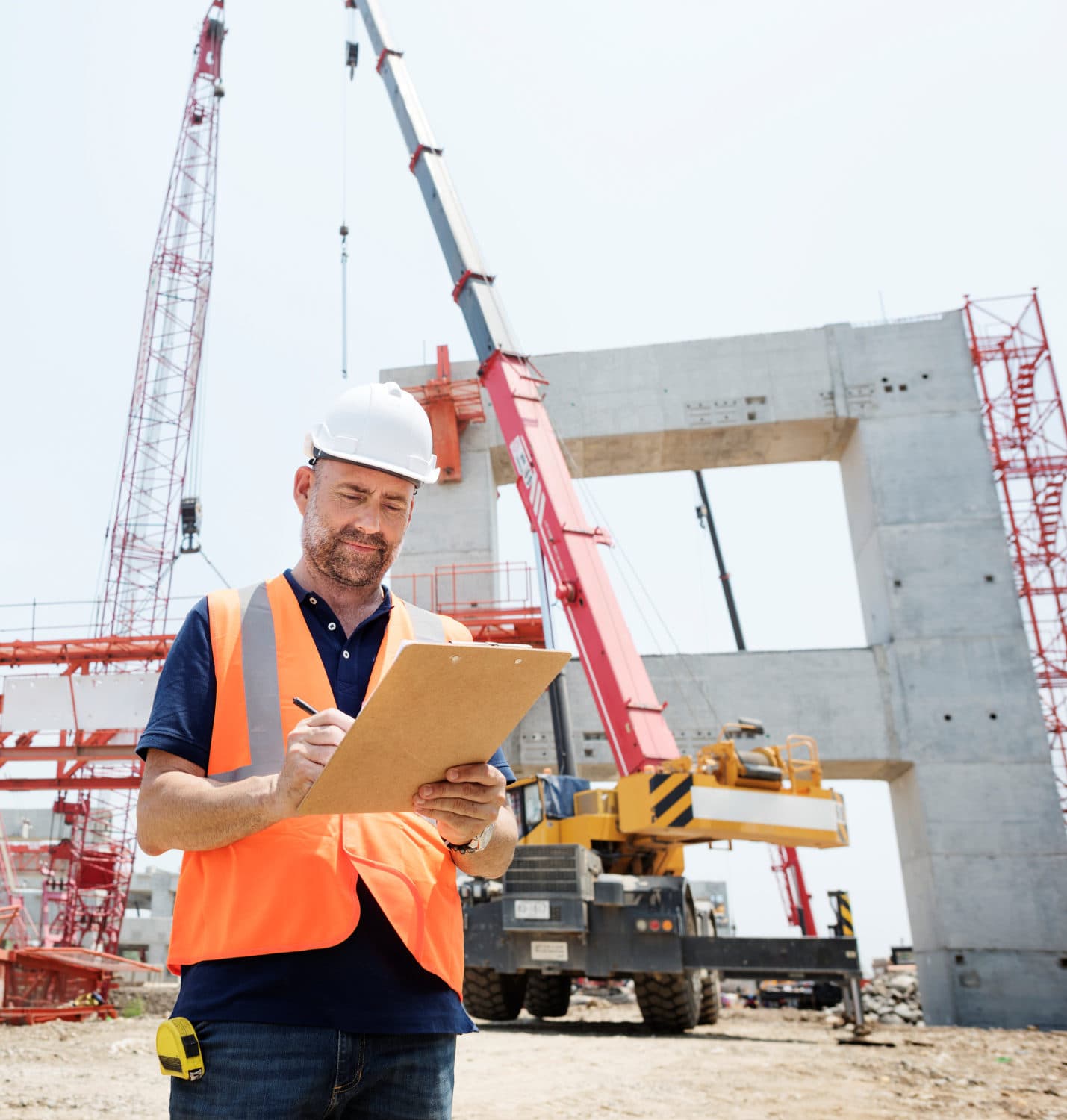 Engineer in a hard hat and orange vest on a construction site with cranes